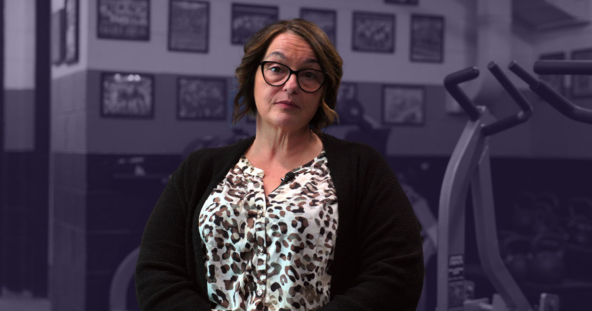Cathy Welsh sits in a football stadium locker room corridor surrounded by pictures of former players.